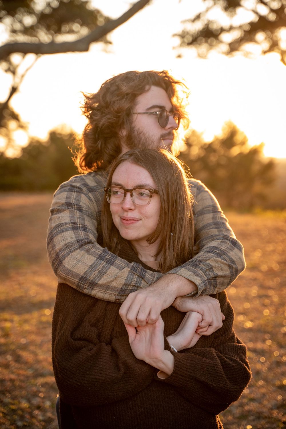 A tender embrace captured in golden sunlight with a plaid shirt and black sweater during sunset.