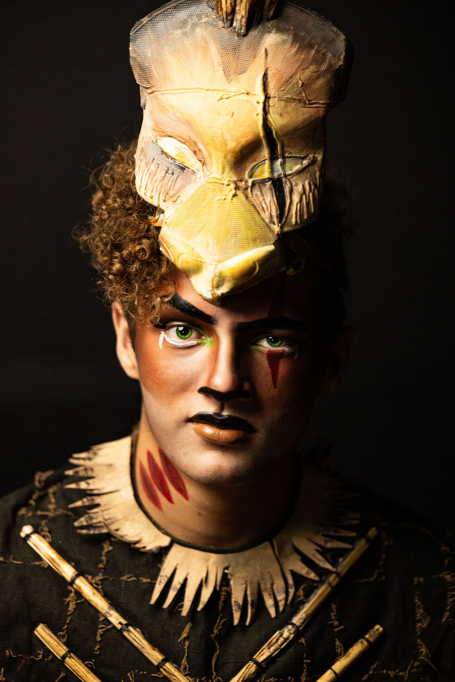 Male performer in Lion King stage makeup with animal skull headdress and warrior costume.