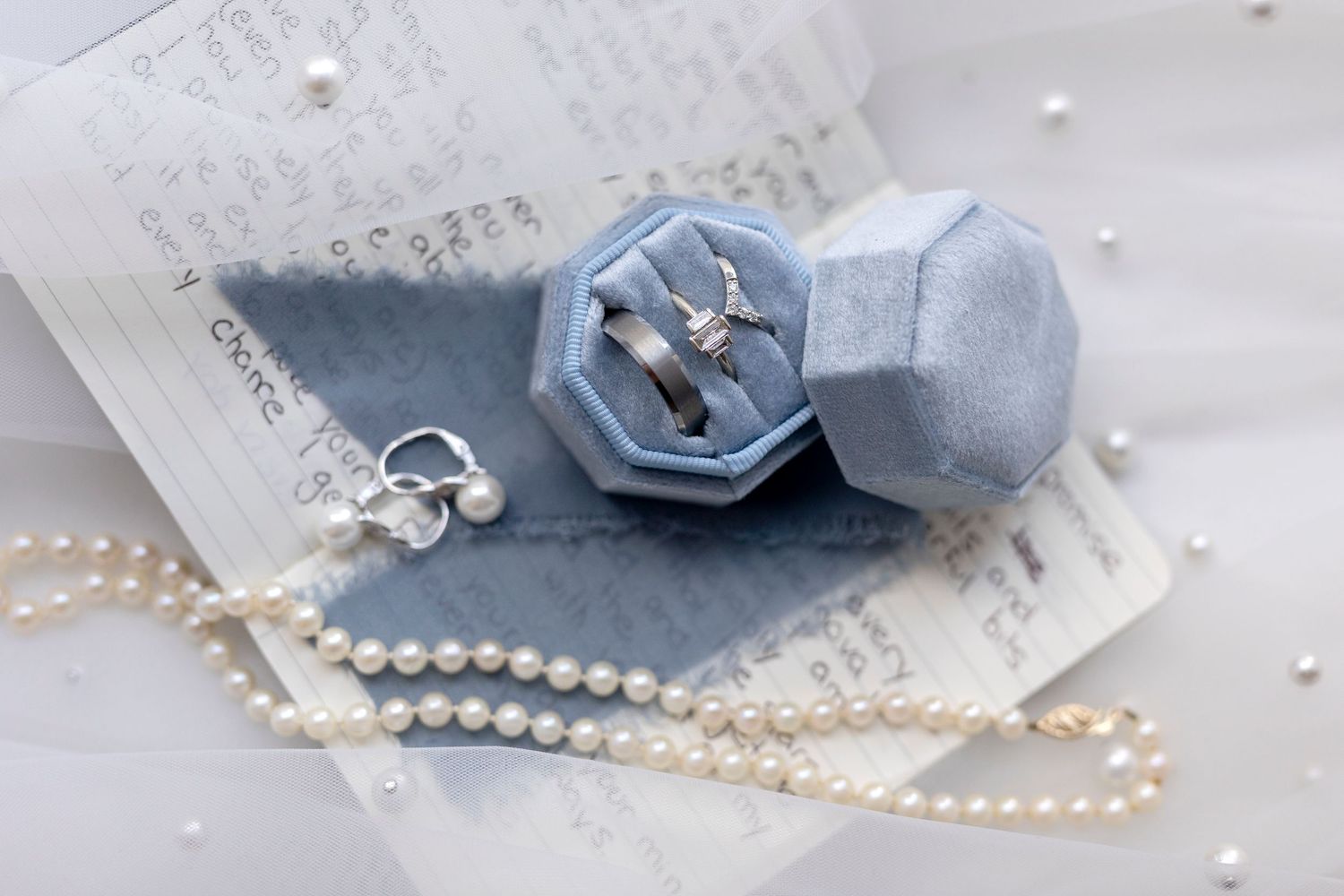 A lay flat design showing wedding rings, pearls and vows.