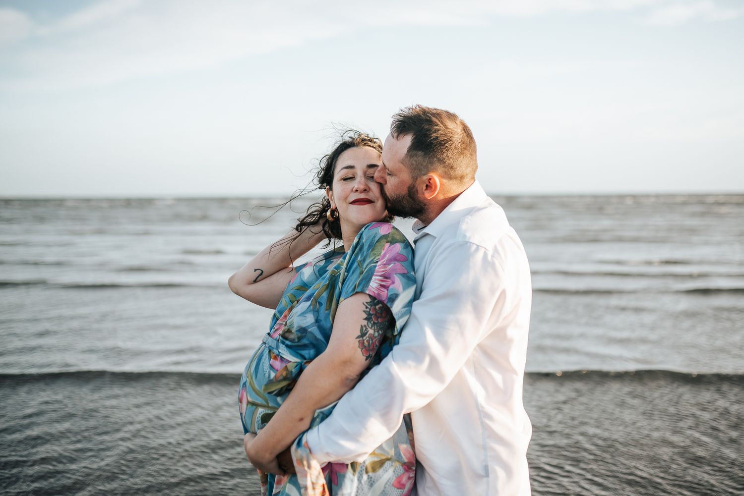 Romantic couple embraces on beach at sunset with ocean waves in background taken by a Melbourne maternity photographer.
