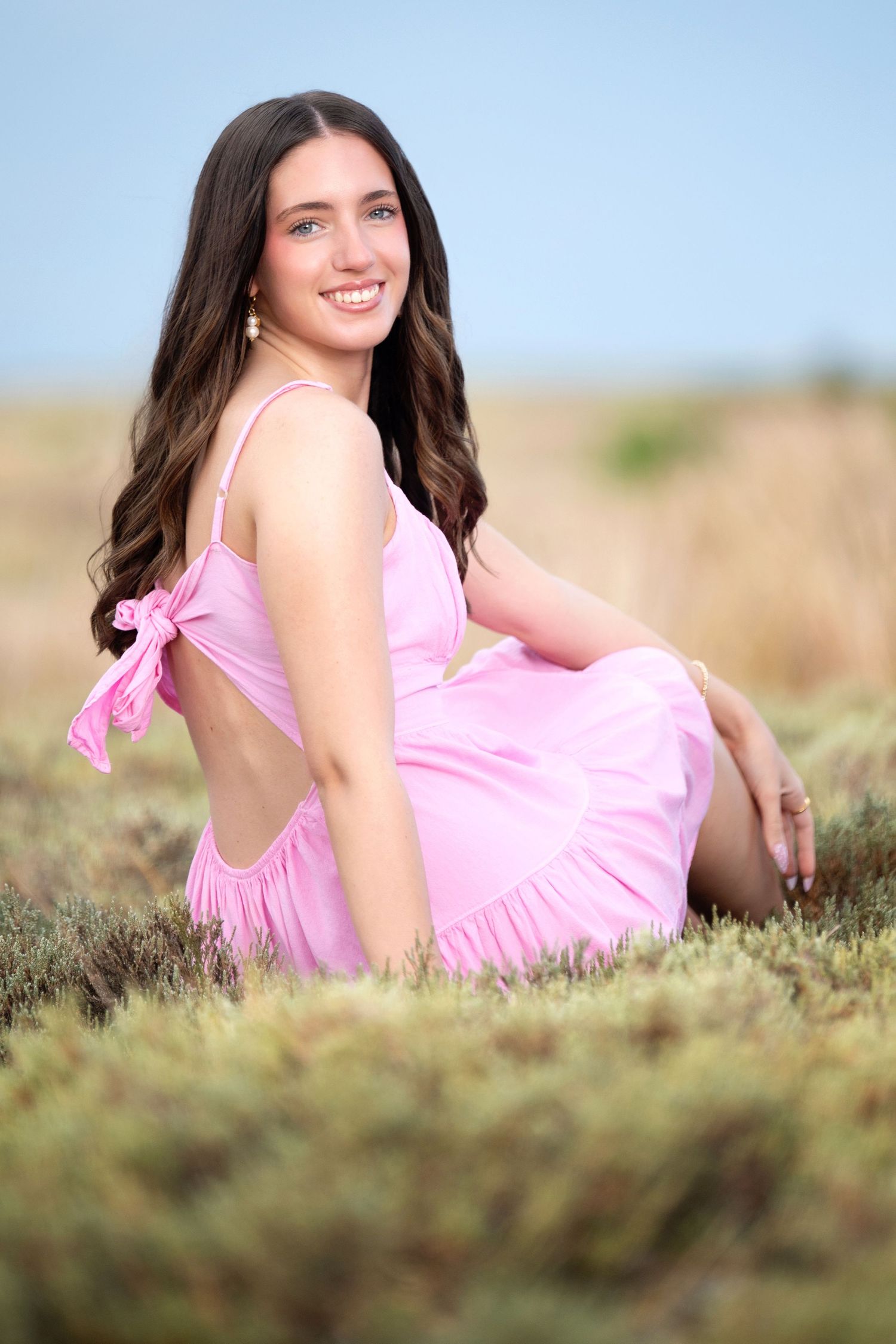 A person in a pink sundress poses gracefully in a natural outdoor setting with tall grass and soft lighting.