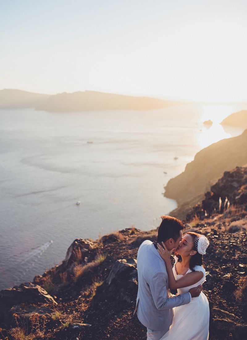 Bride and groom embracing on Santorini cliffs with sea view at sunset