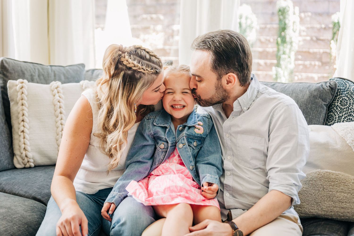A loving family shares tender moments together while sitting on a gray couch in their living room for Charlotte family photos.