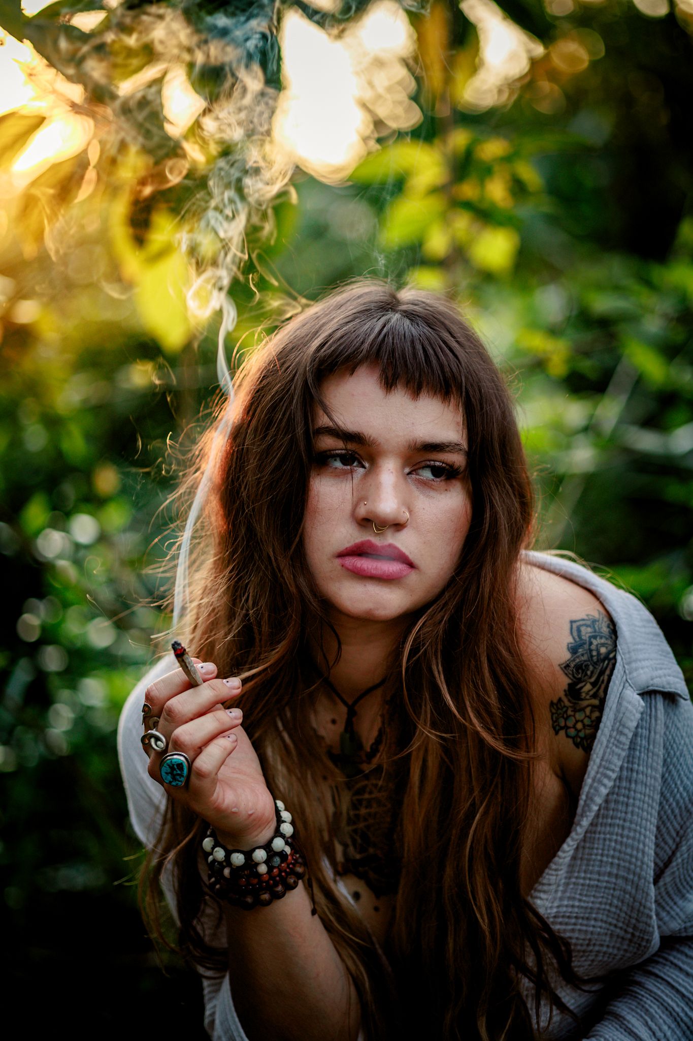 A portrait series of someone with long dark hair and bangs in a grey jacket against a sunlit natural background.