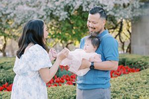 A couple stands together in a garden with red flowers, sharing a joyful moment outdoors on a sunny day.