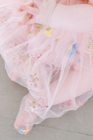 Delicate pink tulle fabric with embroidered floral details and pastel accents creates a dreamy, romantic texture.