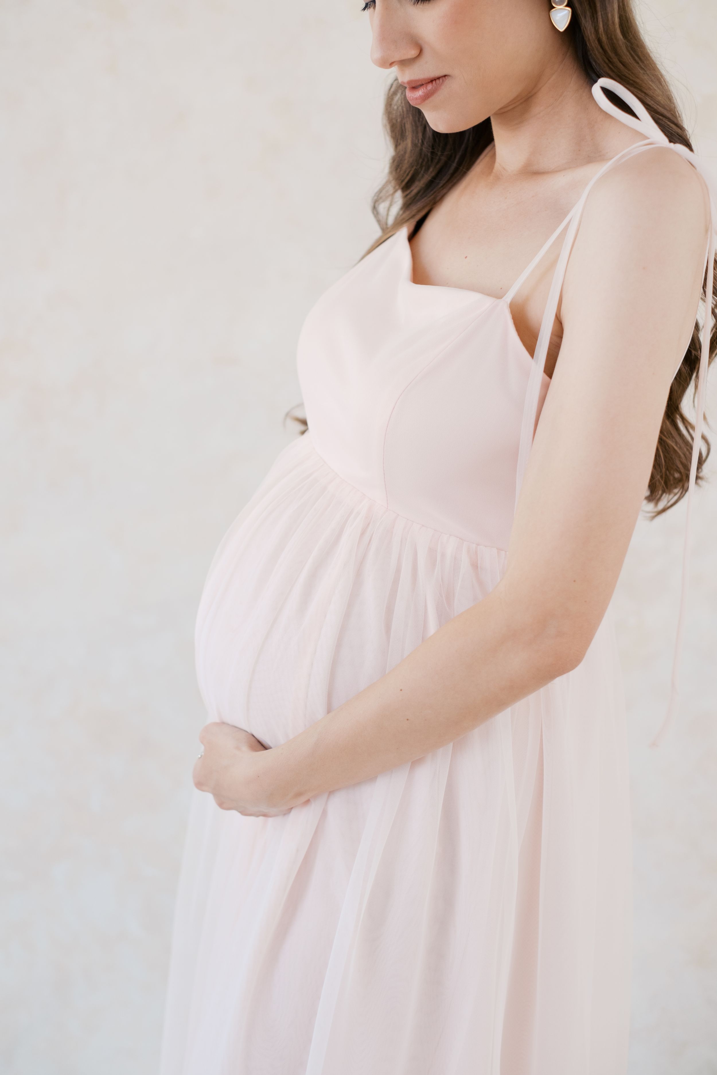 Woman in flowy pale pink sundress poses gracefully against light background in elegant fashion photography series.