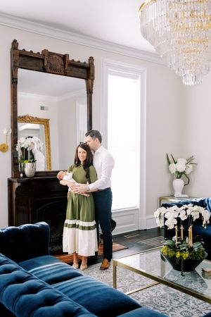 A couple dances together in an elegant room with crystal chandeliers and a plush navy blue velvet couch.