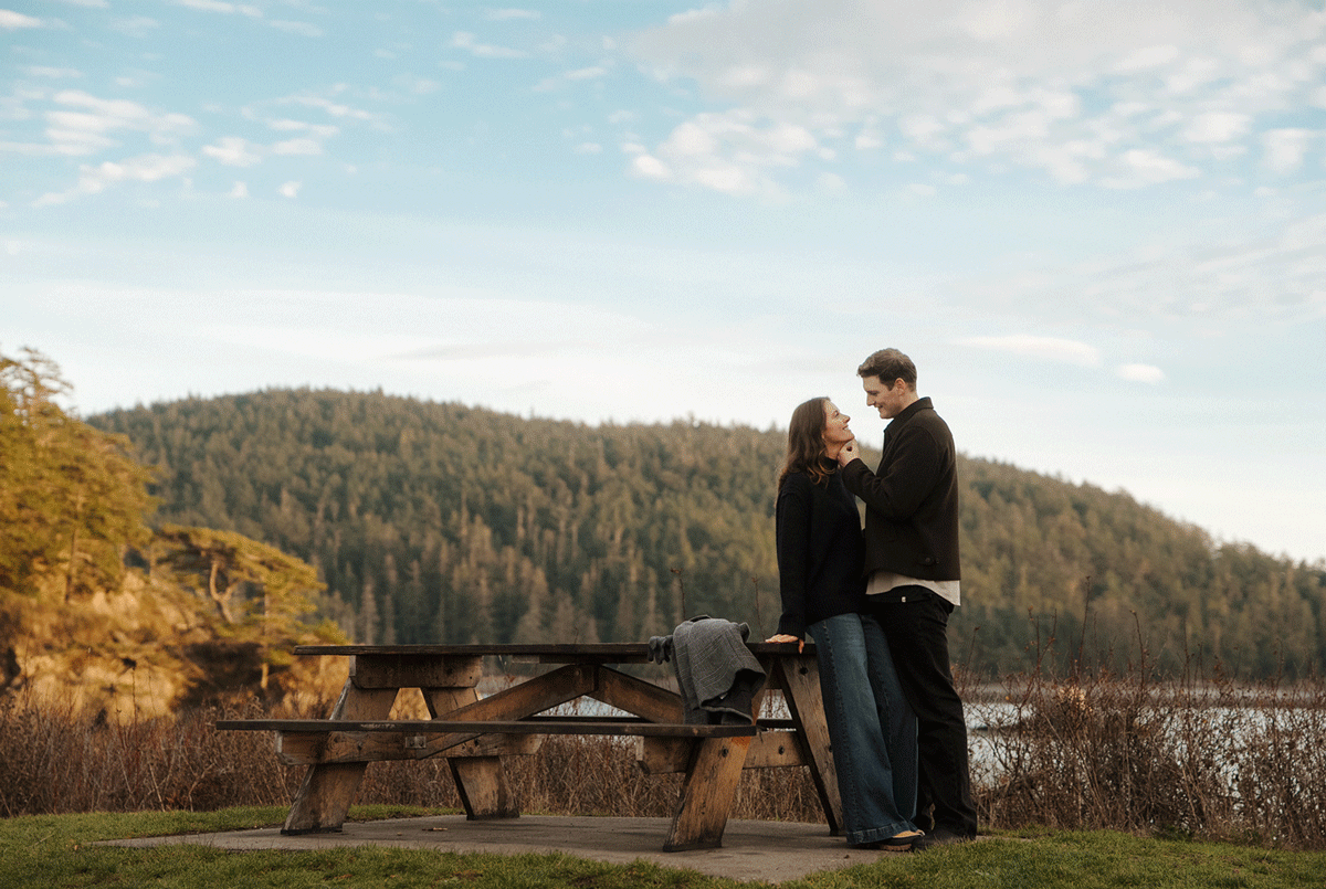 A couple shares a romantic moment at sunset on a mountain overlook with scenic views of rolling hills and autumn foliage.