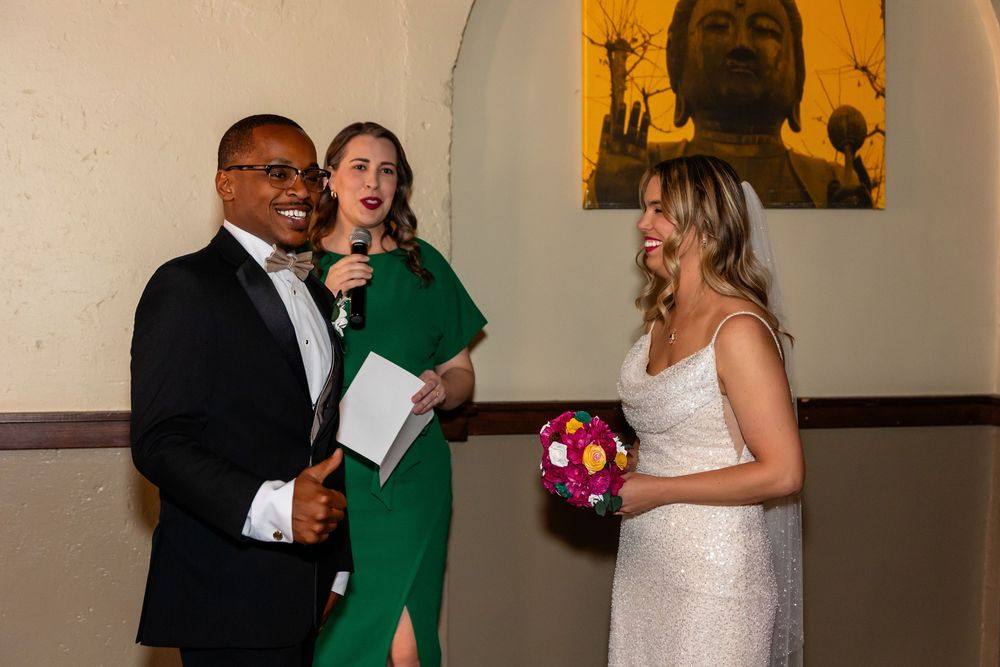 Bride and groom laughing with a female officiant in a green dress during an intimate wedding ceremony  at Blue Sushi in Downtown Omaha, NE