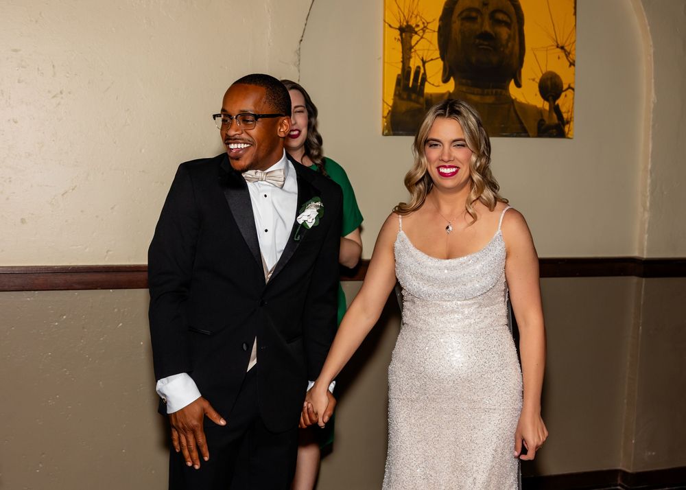 Couple in formal wedding attire smiling and holding hands while making a grand entrance at their reception  at Blue Sushi in Downtown Omaha,