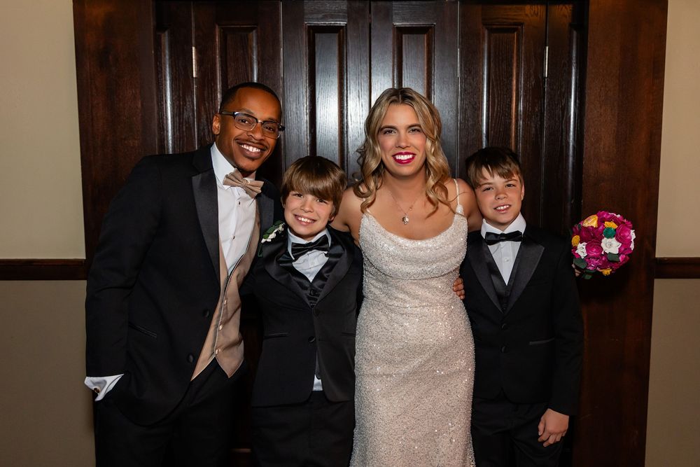 Bride in sequin gown and groom in tuxedo posing with two young boys in suits at wedding reception  at Blue Sushi in Downtown Omaha, NE