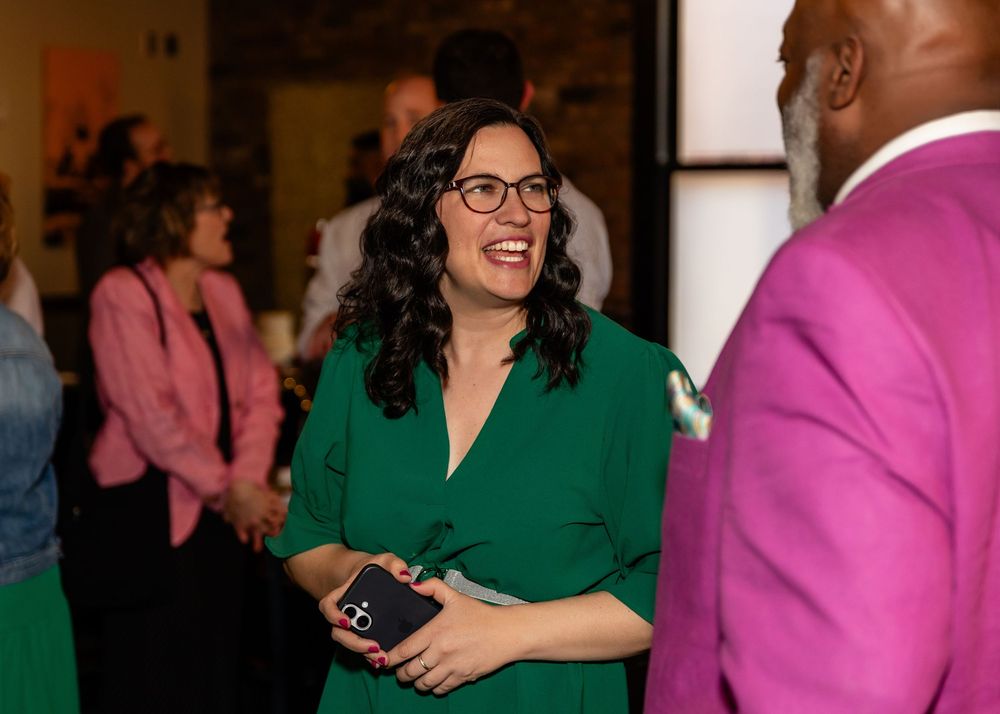 Woman in green dress laughing at wedding reception event with guests in background.