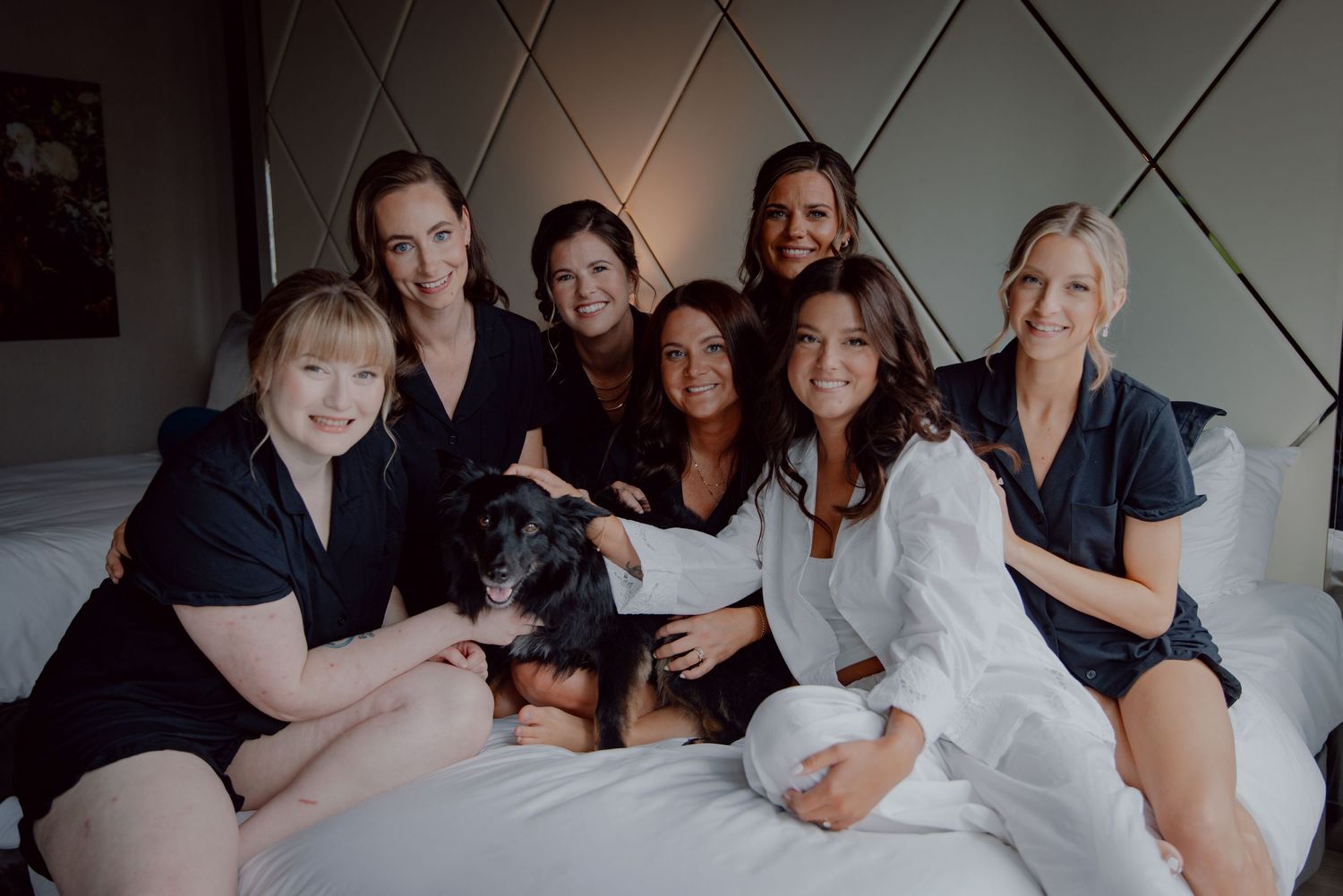 Group photo of friends and dog relaxing together on white bed.