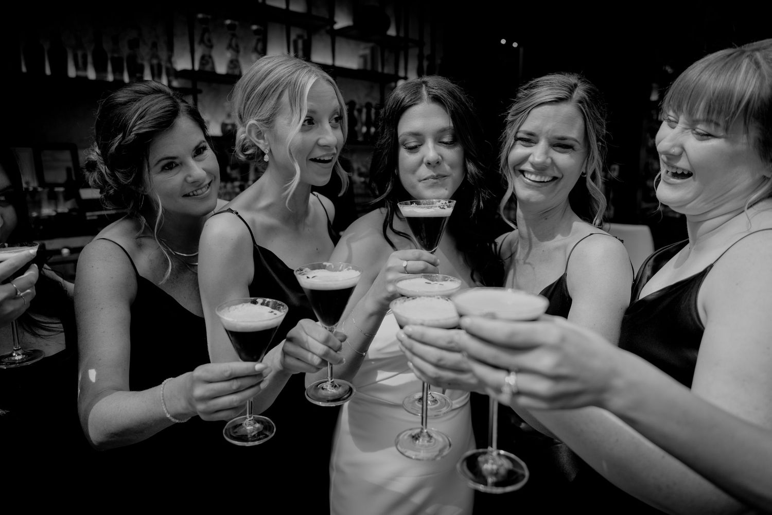 Black and white photo of friends toasting with wine glasses at a celebration.