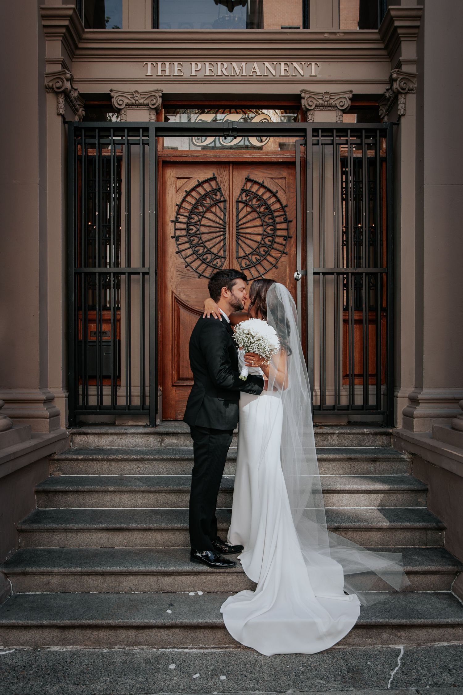 Newlyweds share romantic moment at entrance of The Permanent building.