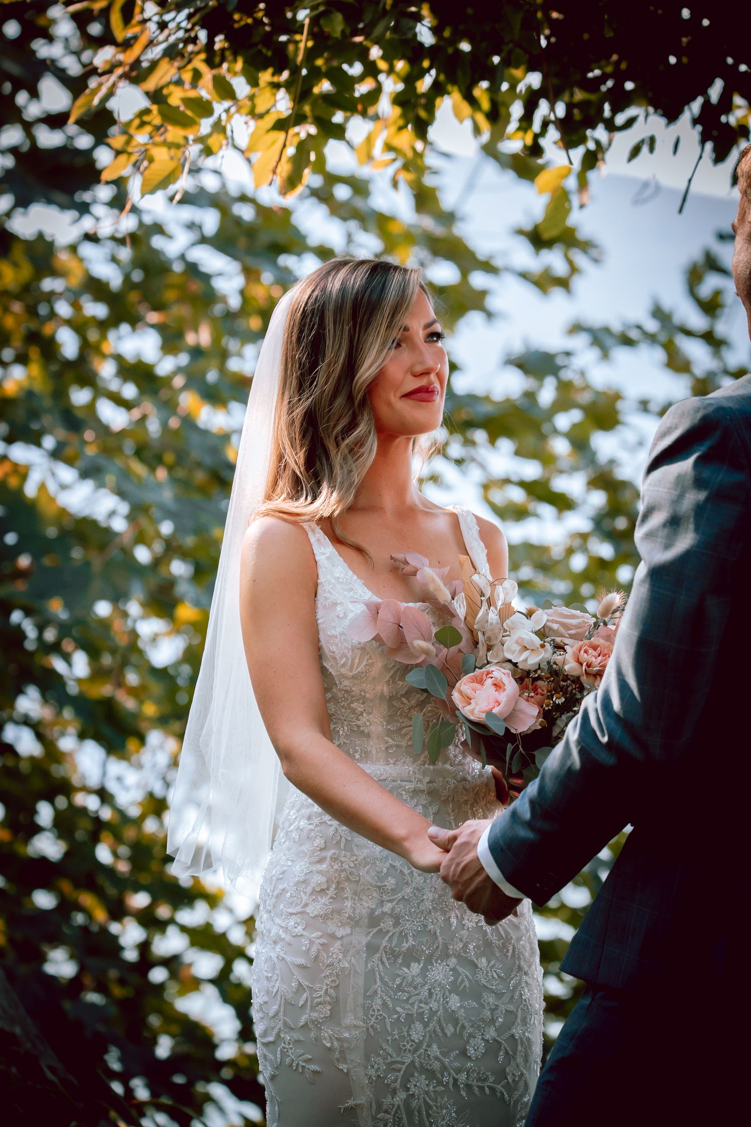 Bride in lace dress holding bouquet during outdoor autumn wedding ceremony.