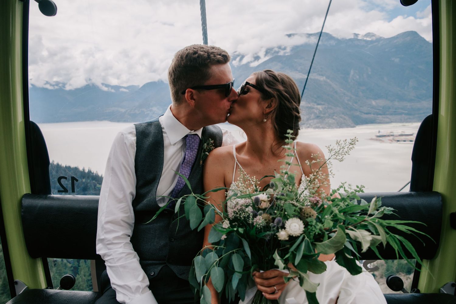 A romantic moment in a gondola with mountain views and white floral bouquet against a scenic backdrop.