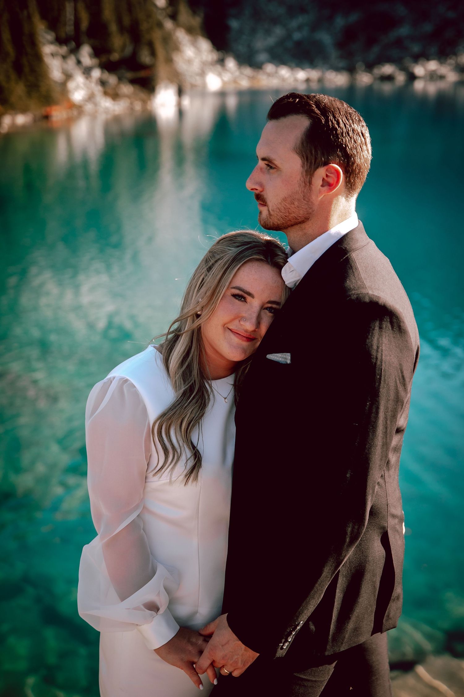 Elegant wedding portrait against backdrop of vibrant turquoise alpine lake.