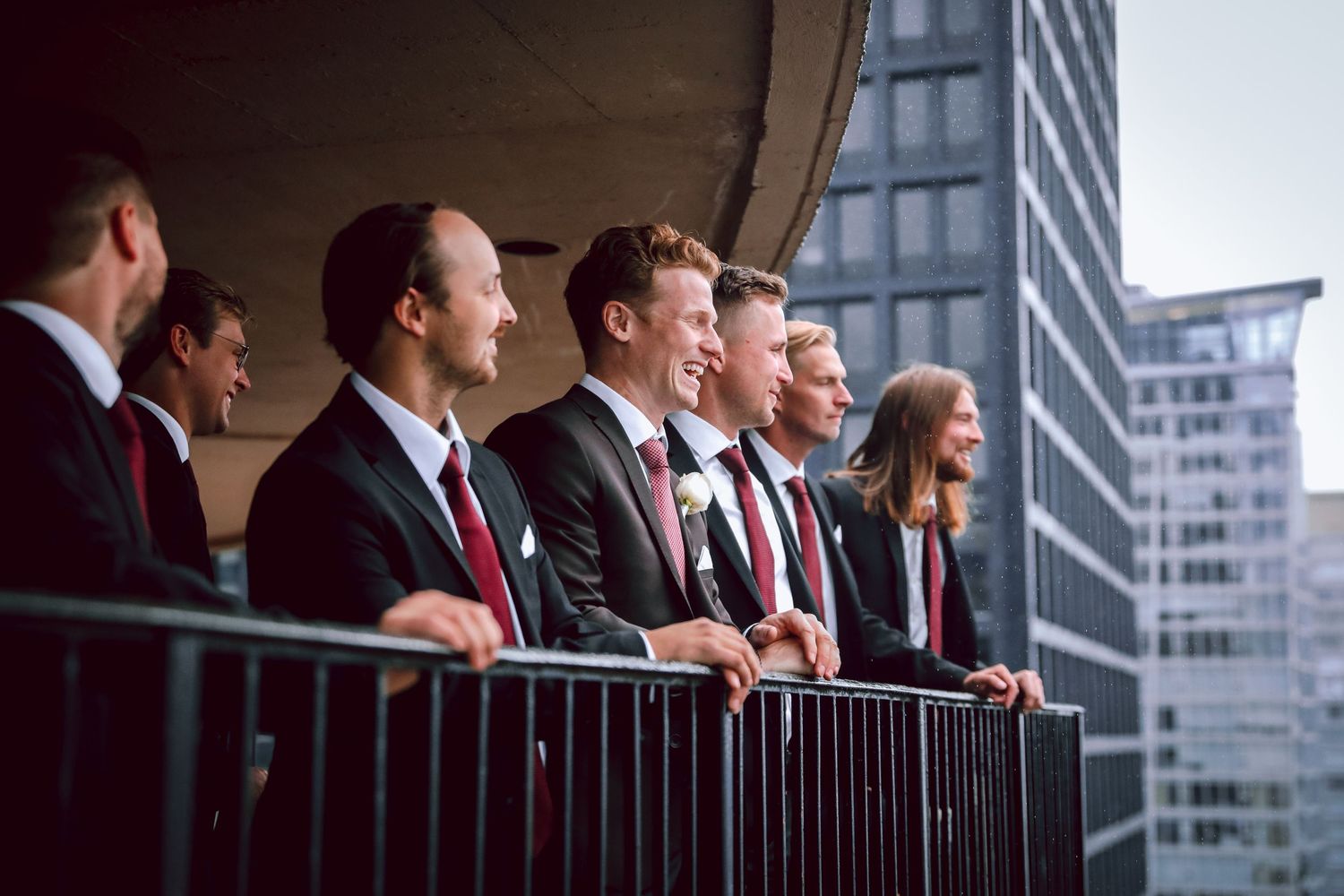 Group of formally dressed people standing on balcony overlooking urban skyline.