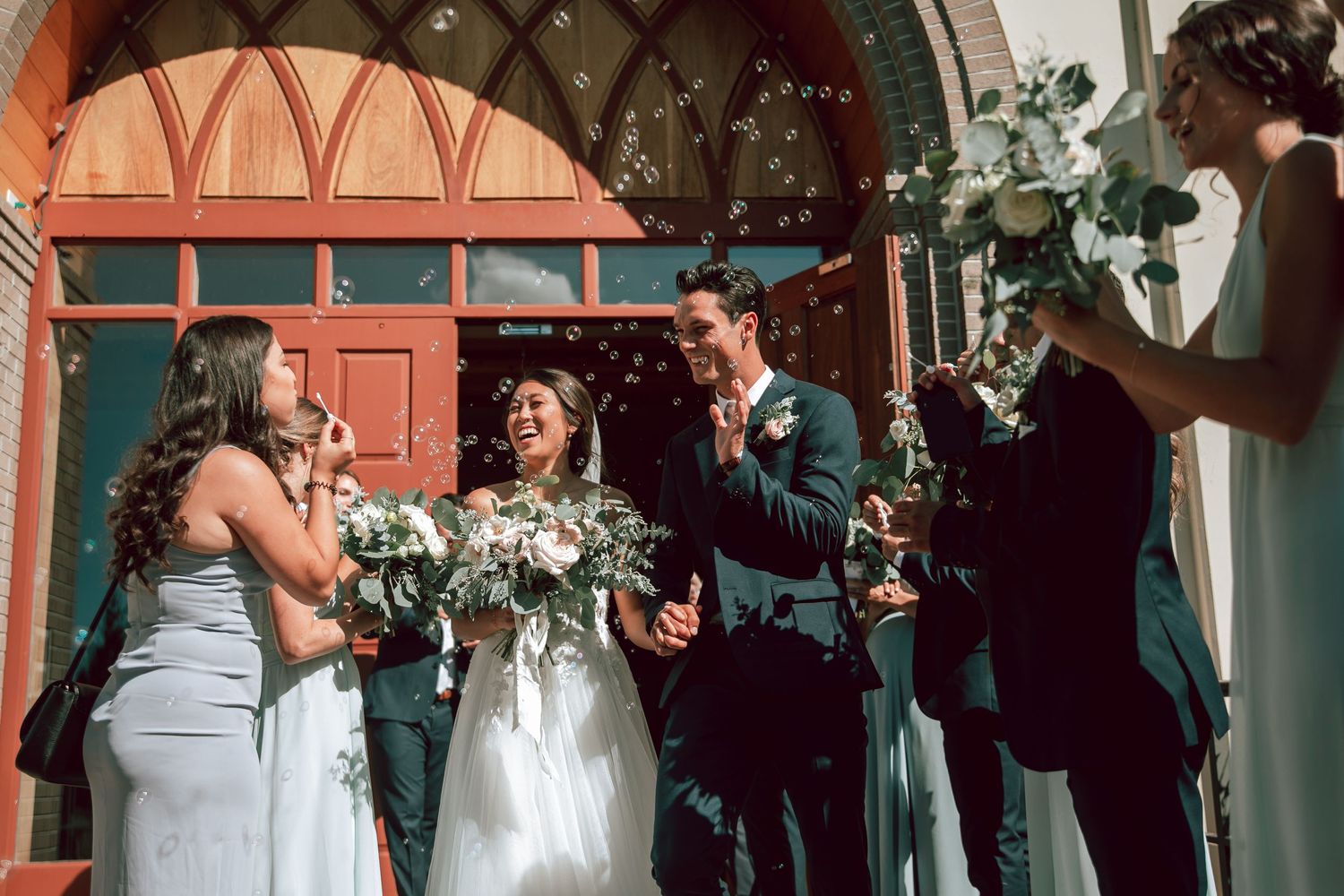Wedding party celebrating outside a historic building with red archway.