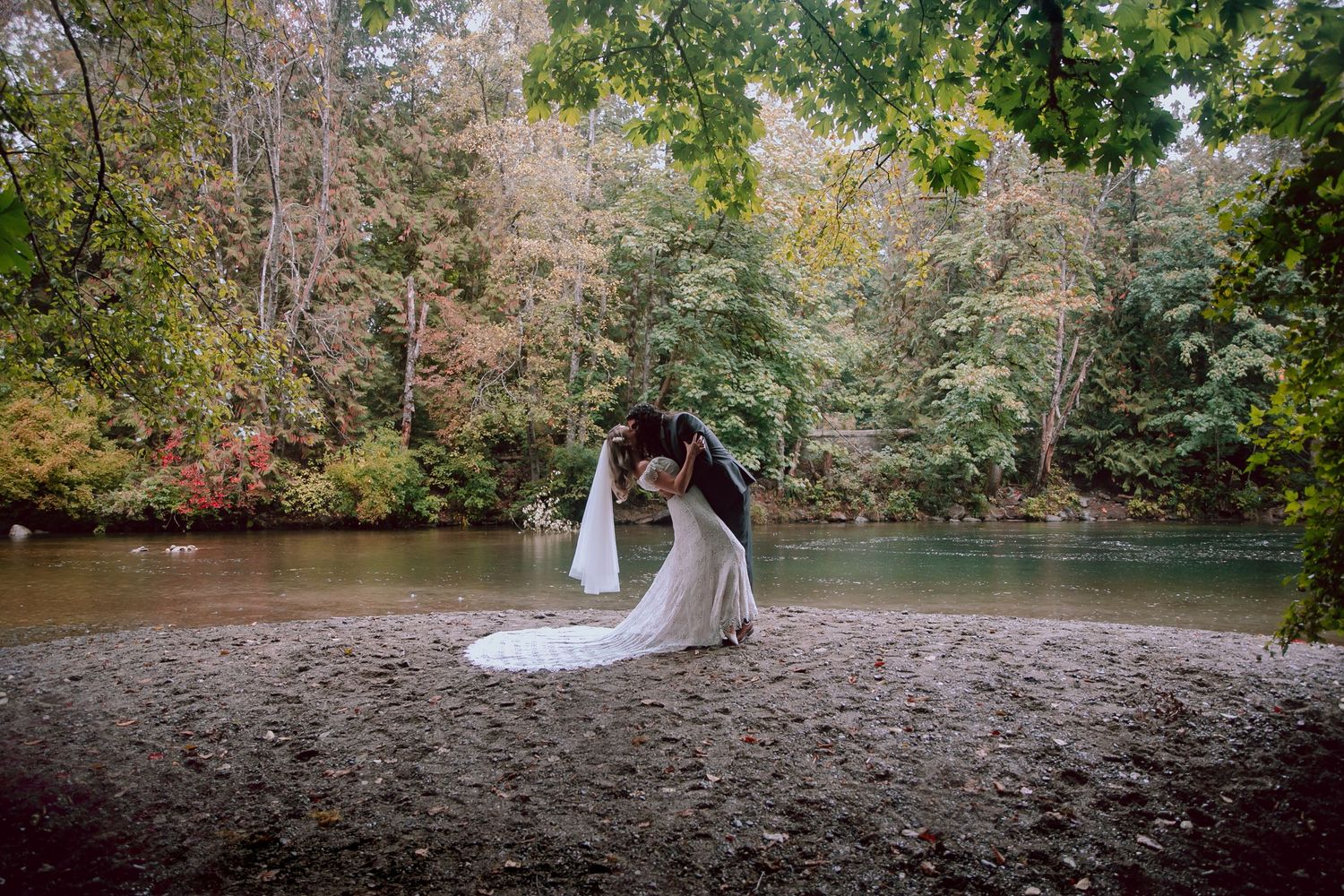 Wedding couple poses together on shoreline of scenic forest lake.