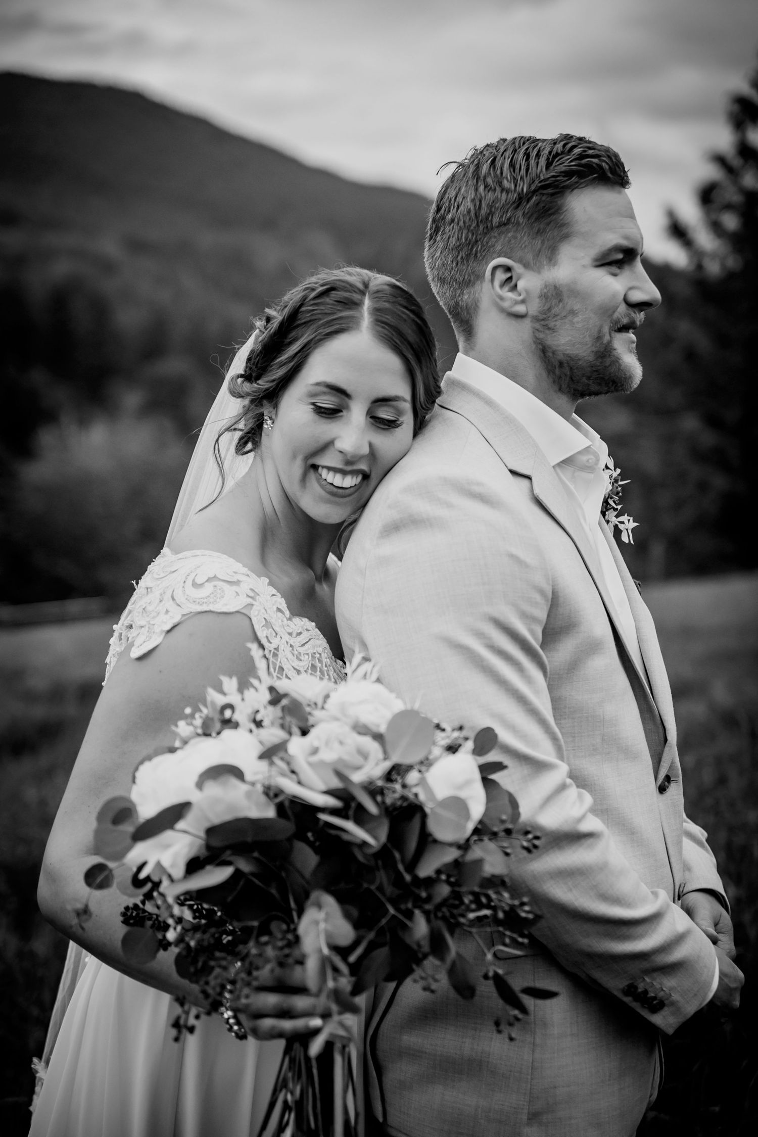 Black and white portrait of a bride and groom in front of mountain landscape with a floral bouquet.