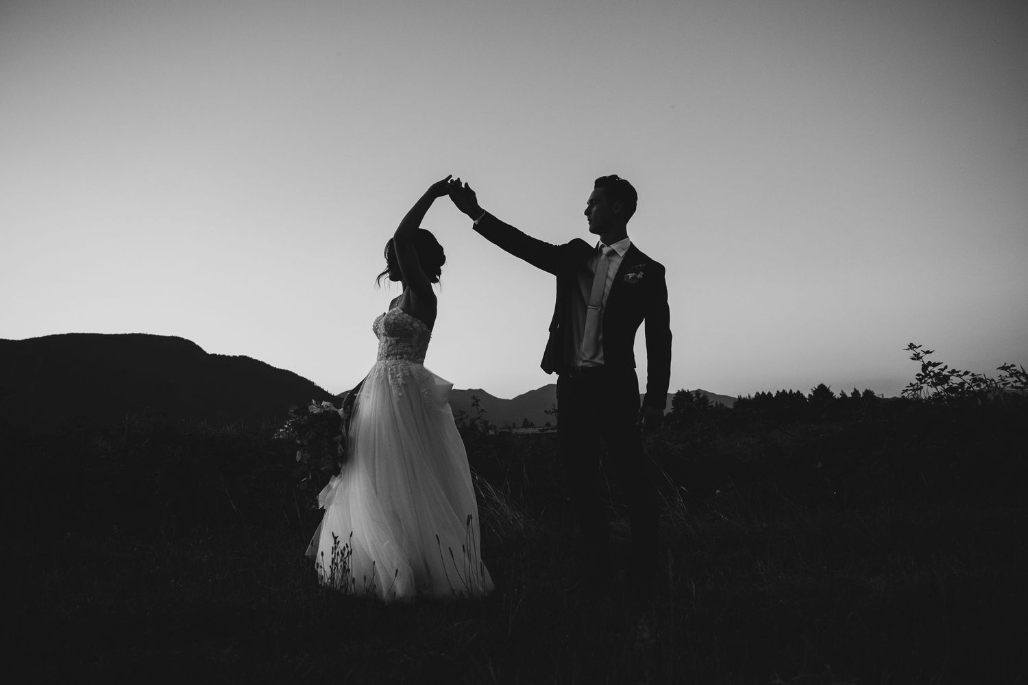 Silhouette of couple dancing at sunset with mountains in background.