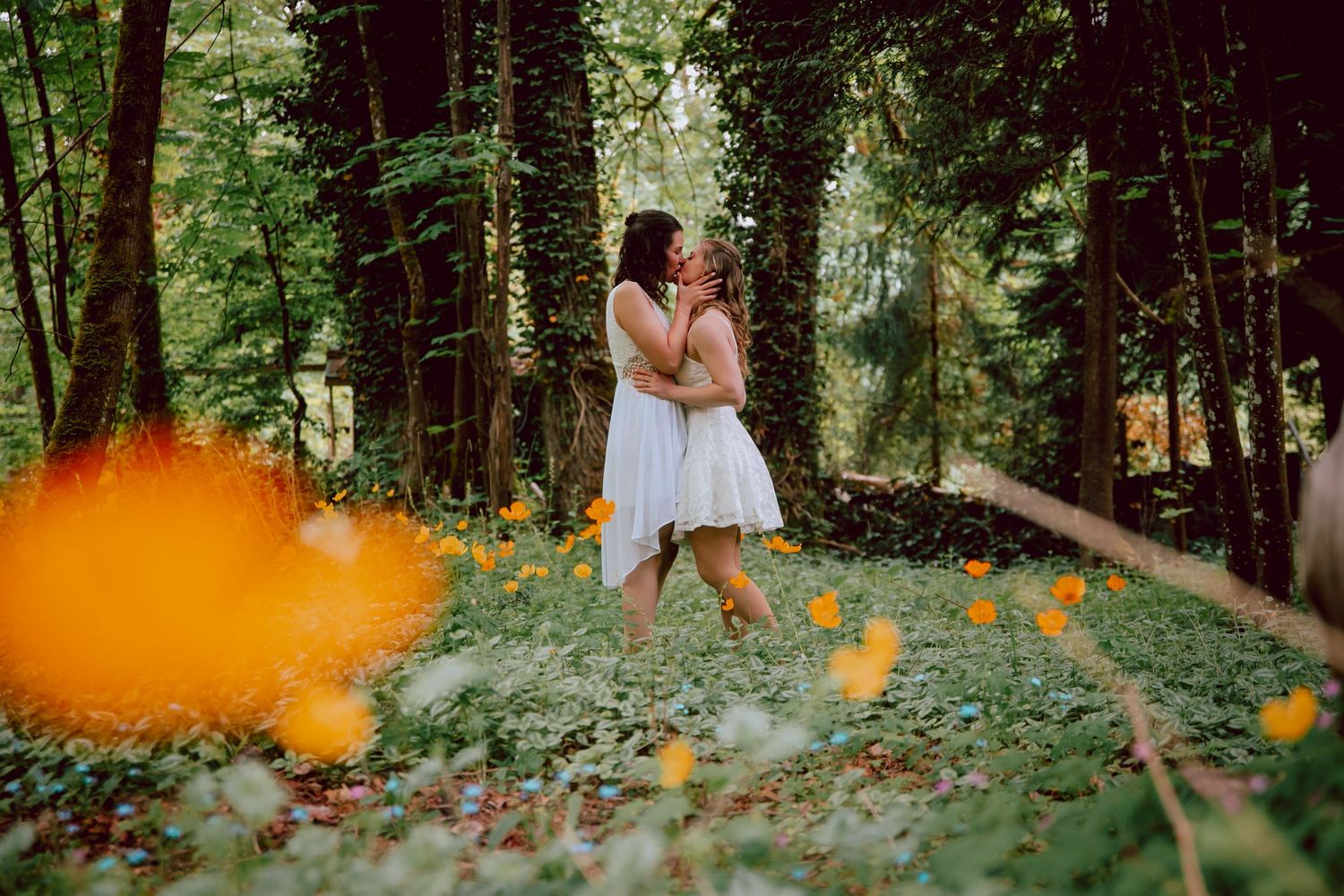 Wedding couple embraces in forest with orange smoke bomb effect in foreground.
