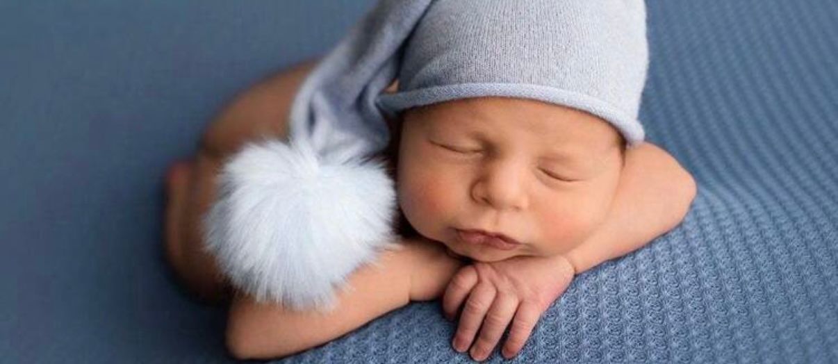 Newborn sleeping peacefully on blue textured surface wearing winter hat.