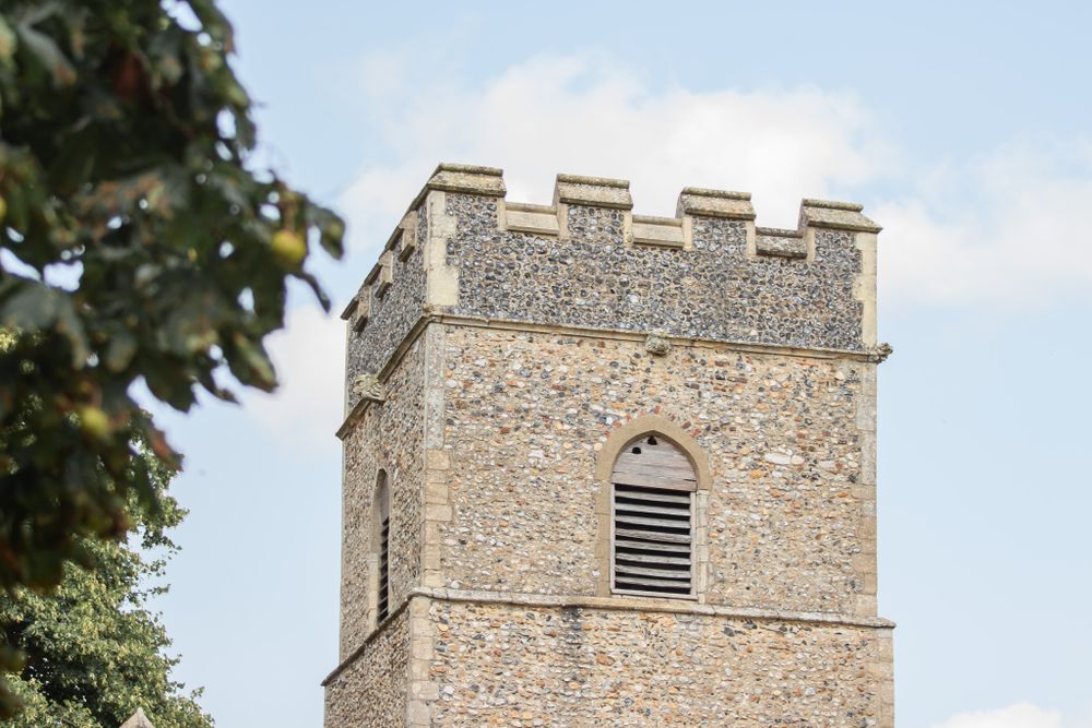 Stone church tower with crenellated battlements and arched window vent rises against blue sky.
