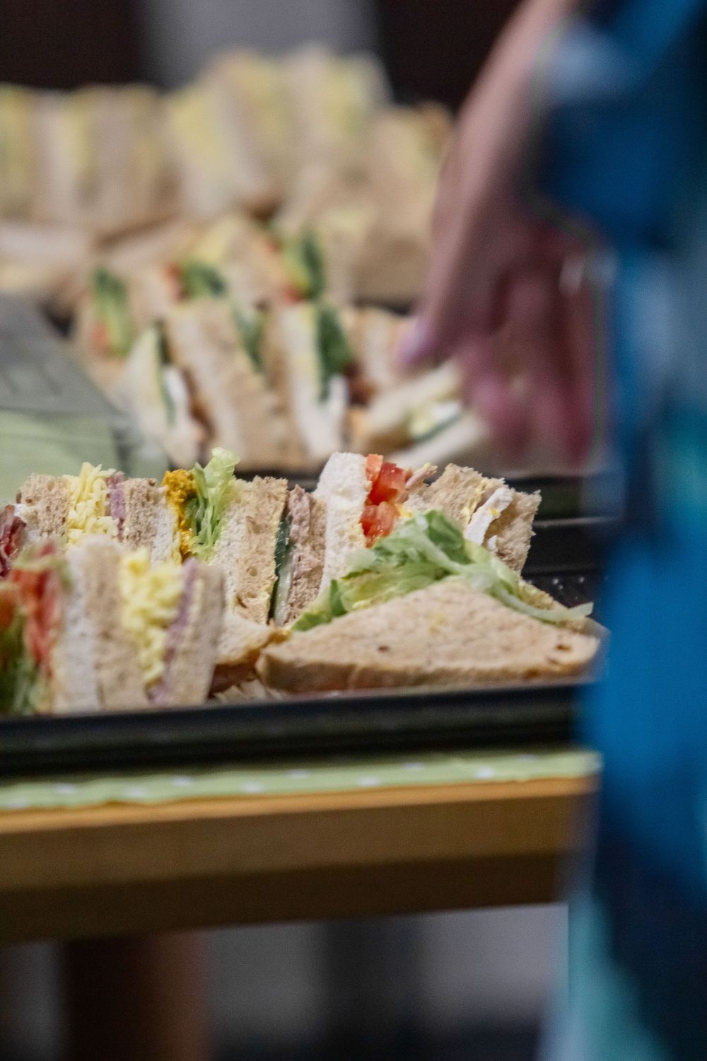 Close-up of layered club sandwiches stacked on a dark serving platter with fresh lettuce and colorful fillings visible.