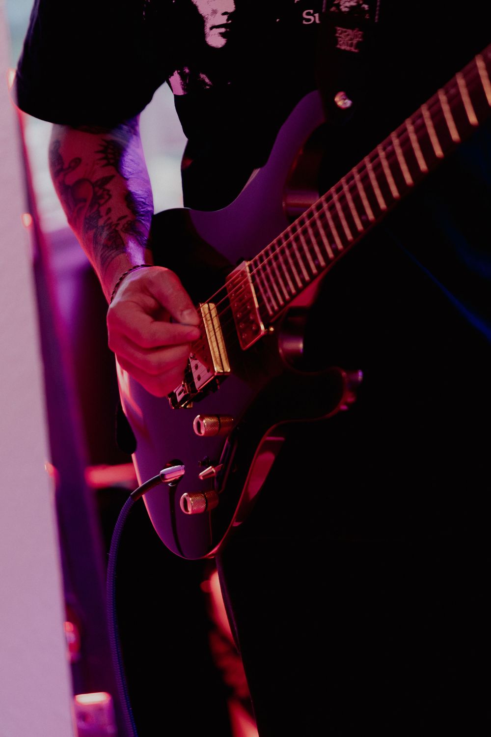 Close-up shot of electric guitar being played under purple stage lighting during a live performance.