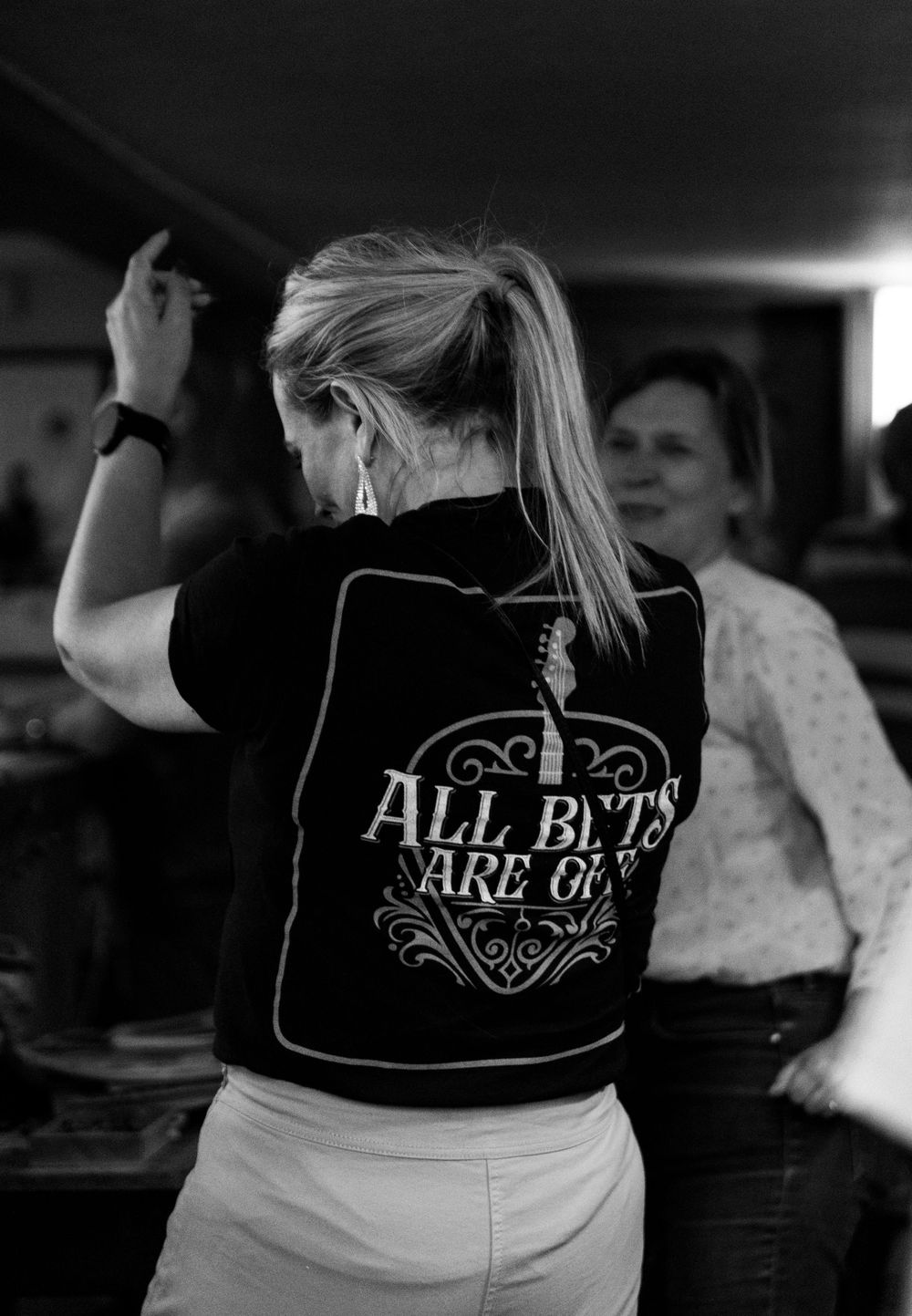 A series of black and white photos showing text on t-shirts that read 'ALL BETS ARE OFF' in a bar setting.