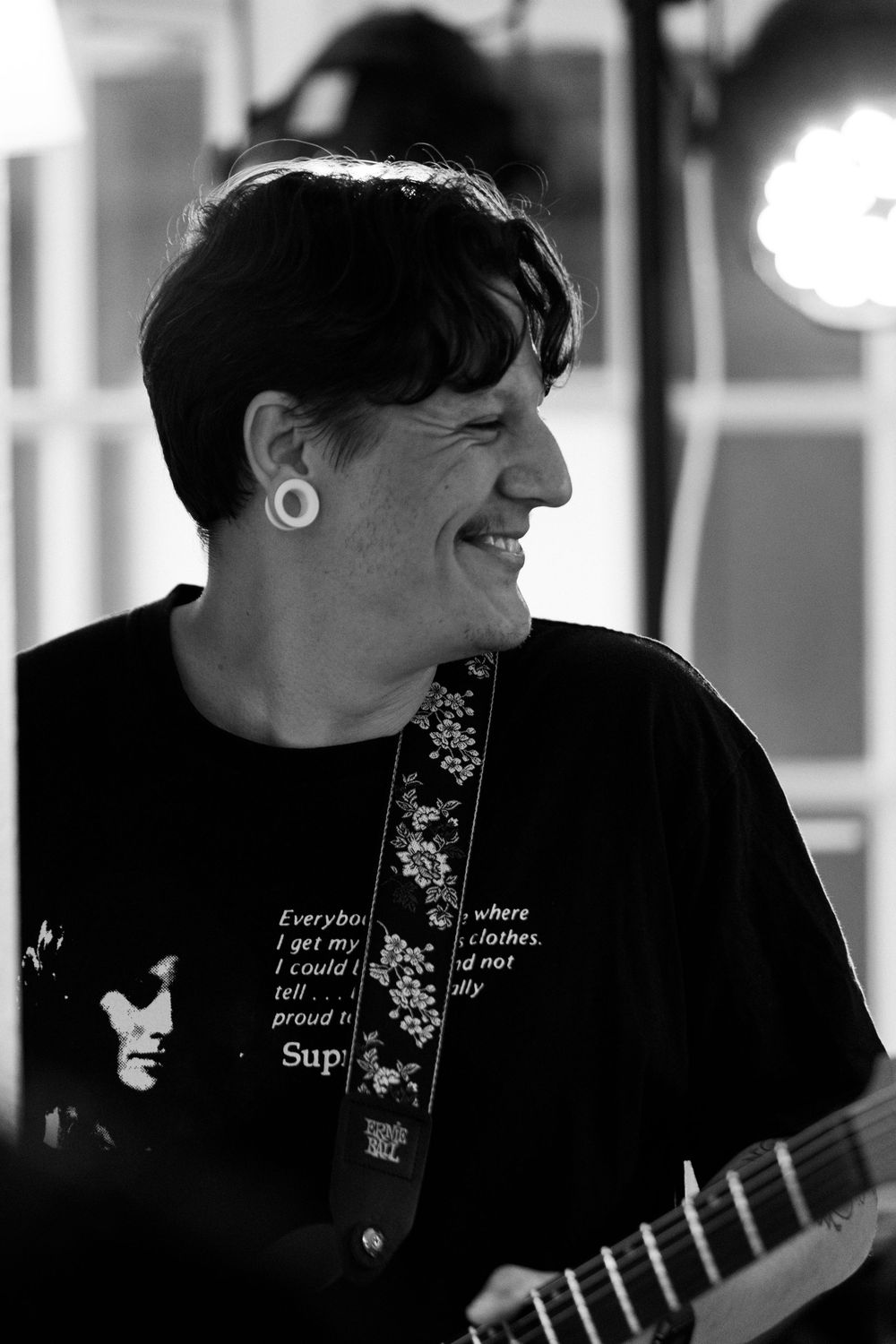 A black and white photo of someone playing guitar while wearing a dark t-shirt with text and floral designs.