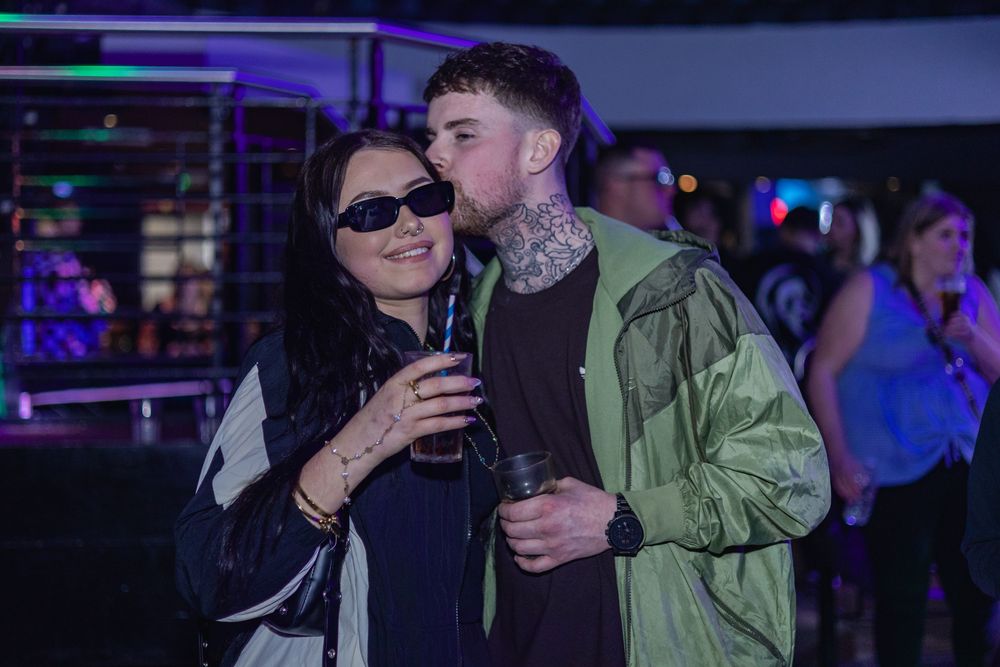 People dancing and socializing at a nightclub with colorful neon lighting and dark ambiance.