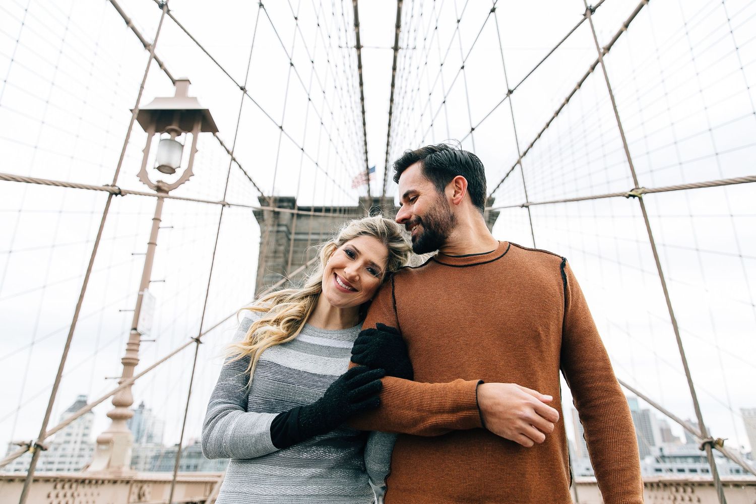 Couple shares a romantic moment on the Brooklyn Bridge with city views in the background.