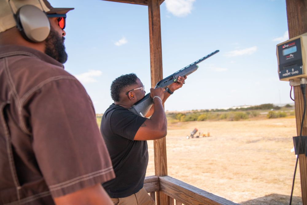 Shooter taking aim at clay target from covered shooting station.