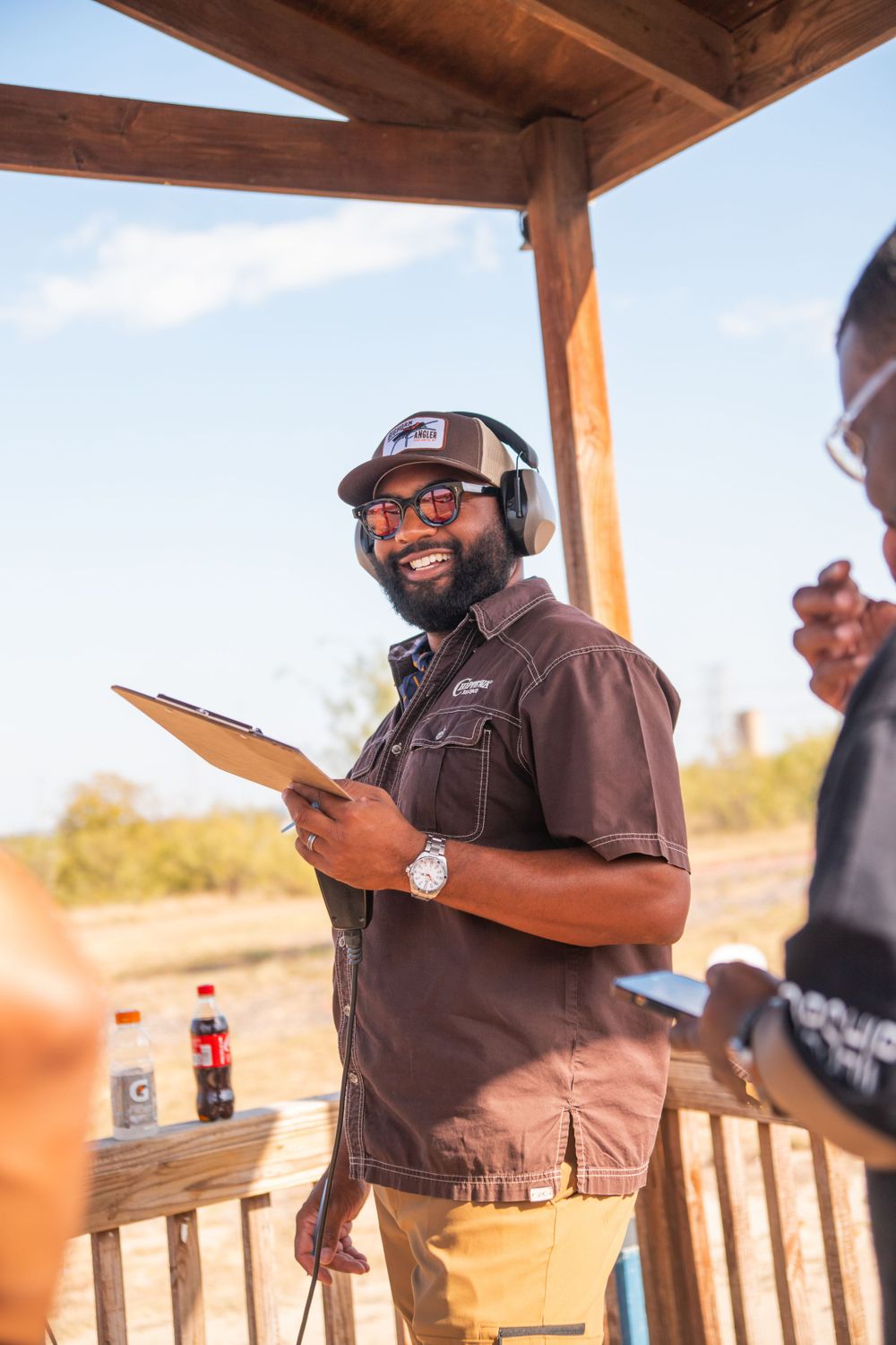 Staff member with clipboard and hearing protection at outdoor shooting range.