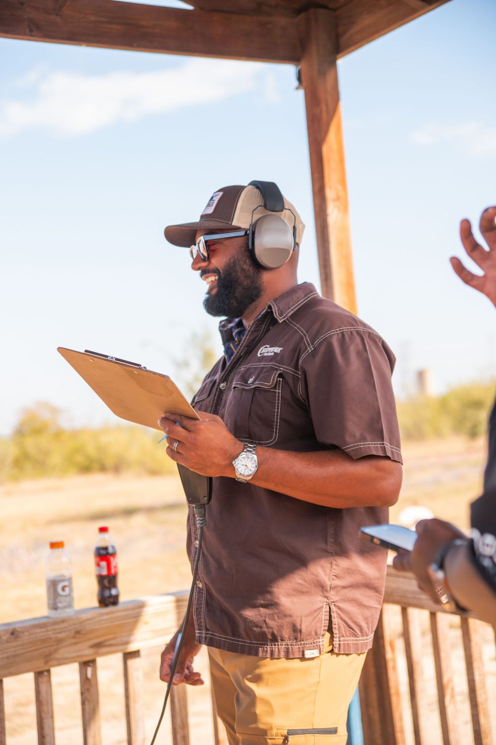 Staff member with clipboard and hearing protection monitoring shooting range activities.