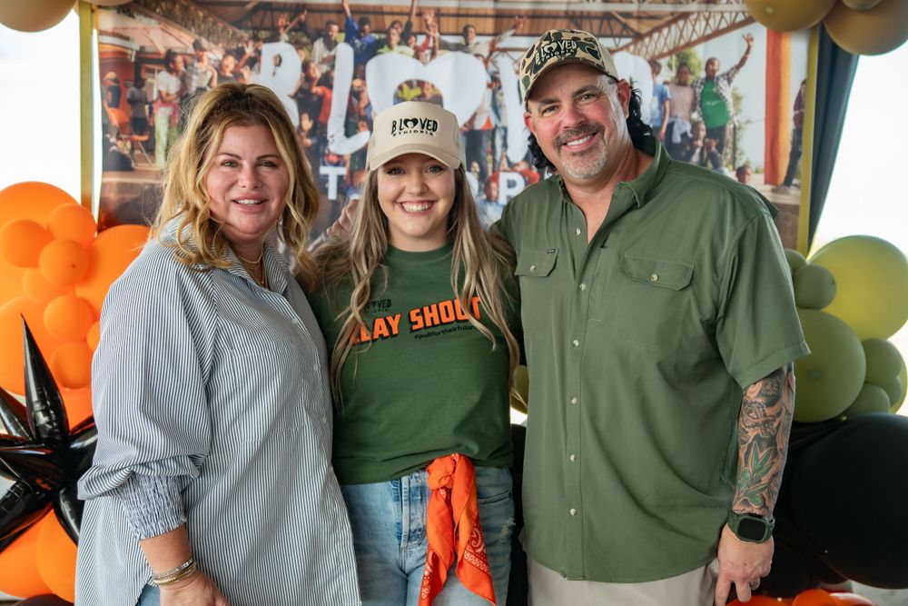Three people pose together at an event with orange and green balloons in the background.