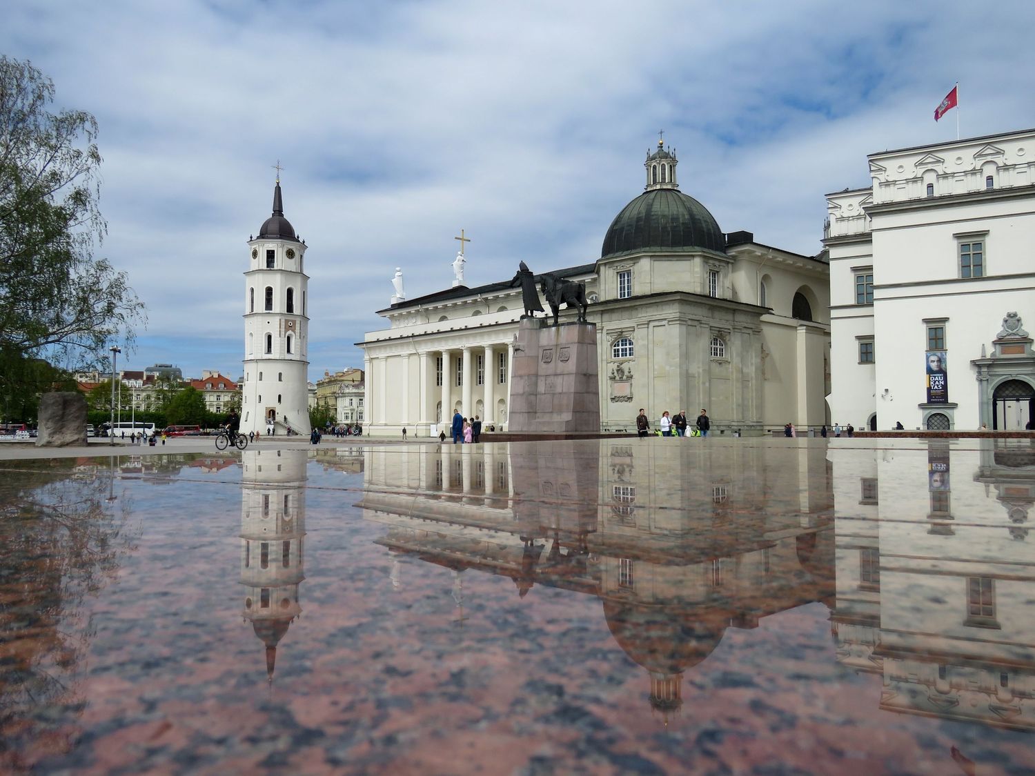 Cathedral Square in Vilnius with reflective wet pavement and classical architecture under cloudy sky.