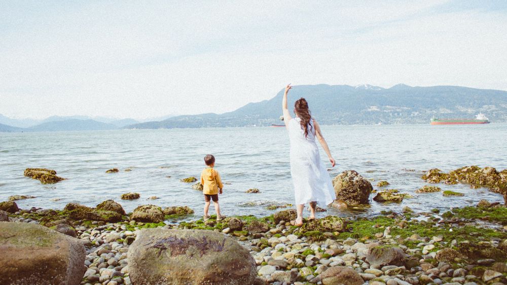 mommy and me photo session at the beach in vancouver, bc with the two of them throwing rocks into the ocean together.