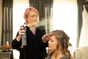 Stylist applies hairspray while finishing wedding day hairstyle preparation.
