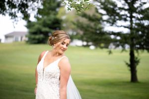Bride in lace wedding gown poses in a serene outdoor setting with rolling hills in background.