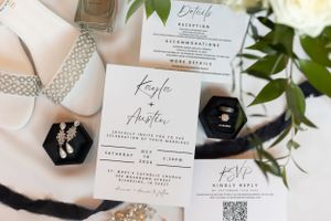 Elegant wedding invitation suite with black accents and floral details displayed with rings.