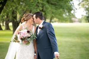 Couple shares intimate moment on their wedding day in a lush garden setting with pink floral bouquet.