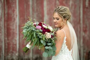 Wedding portrait of bride with burgundy and blush bouquet against rustic red barn.