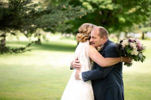 Wedding couple embraces on grassy lawn during outdoor celebration.