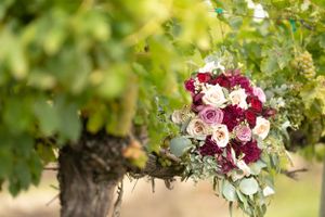 Romantic burgundy and blush wedding bouquet with roses and eucalyptus hanging in garden setting.